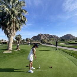 Playing golf in a white dress and navy cap on a desert course