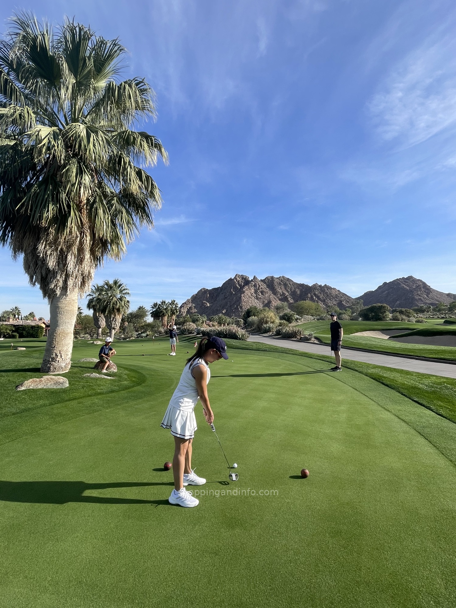 Playing golf in a white dress and navy cap on a desert course