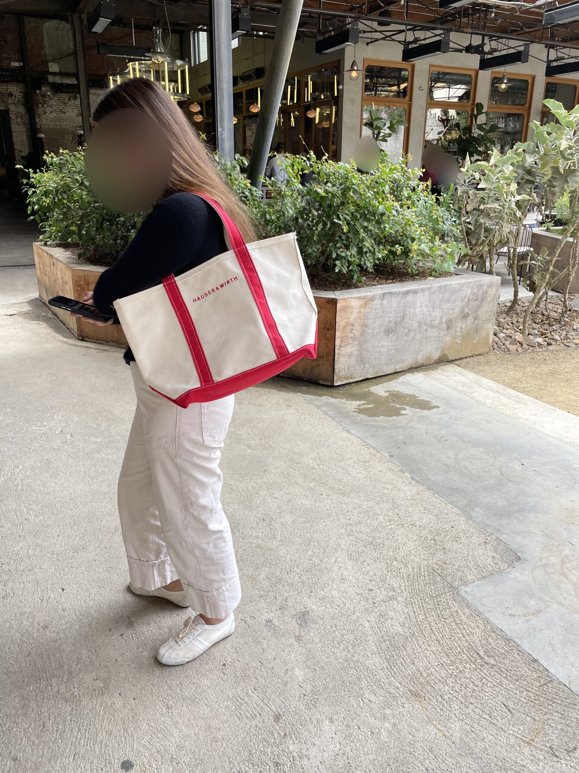A visitor with a cream and red Hauser and Wirth tote in the downtown LA courtyard; faces obscured